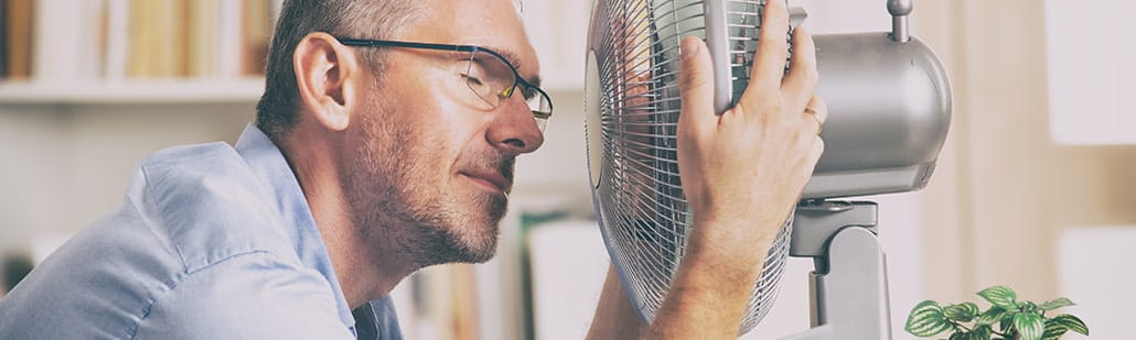 Mann ganz nah vor einem Ventilator, um sich abzukühlen.